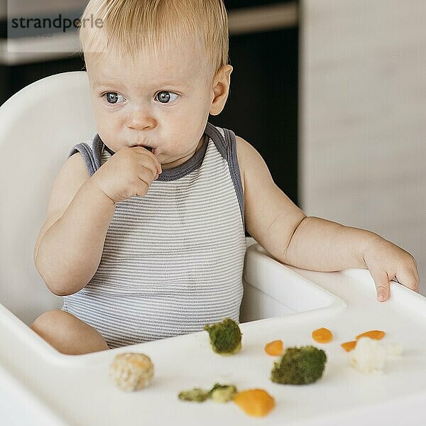 Niedlicher Baby Hochstuhl beim Essen von Gemüse