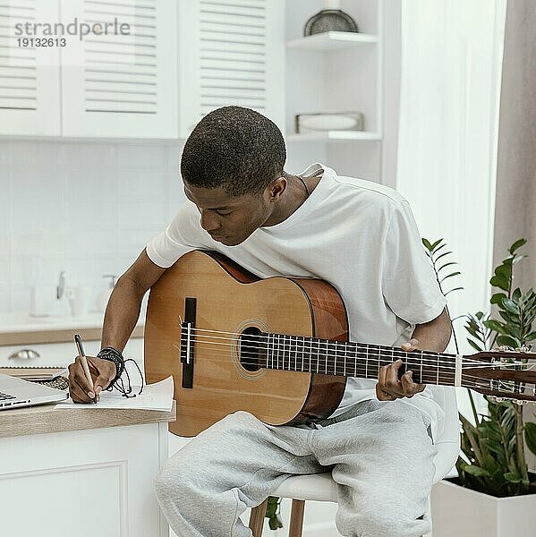 Vorderansicht männlicher Musiker zu Hause  der Gitarre spielt und Texte schreibt