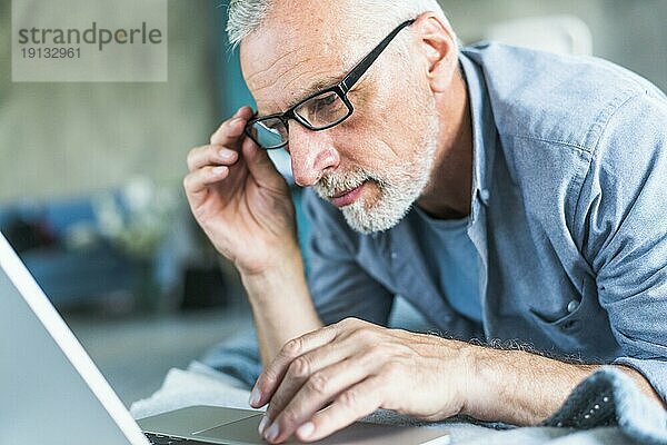 Älterer Mann mit Handbrille schaut auf Laptop