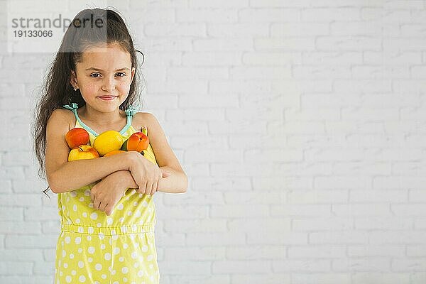 Lächelndes Mädchen hält bunte Früchte in ihren beiden Armen