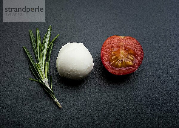 Grüne Rosmarinhälfte fröhliche Tomate Mozzarella Käse schwarze Oberfläche