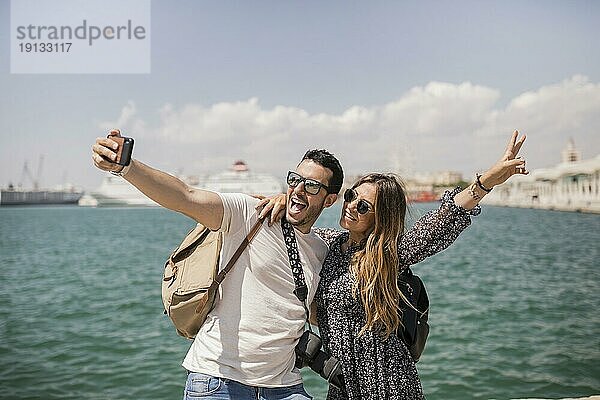 Frau macht Friedenszeichen mit ihrem Freund  der ein Selfie mit dem Handy macht