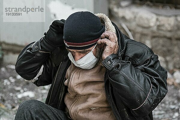 Vorderansicht Obdachloser Mann im Freien  der eine medizinische Maske aufsetzt