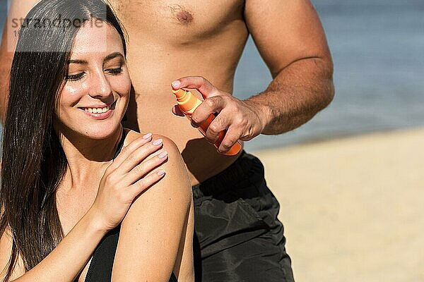 Mann hilft Frau beim Auftragen von Sonnenschutzmittel am Strand
