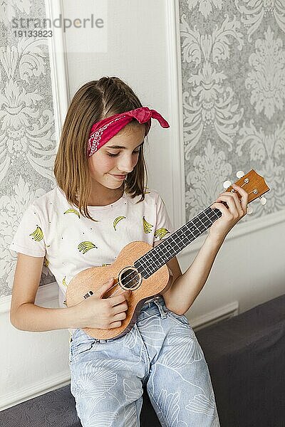 Lächelndes kleines Mädchen spielt Ukulele zu Hause