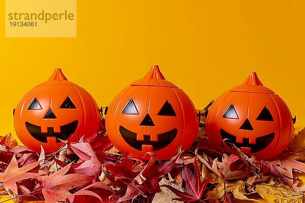 Halloween orange Kürbisse auf einem gelben Hintergrund  verziert mit roten Herbstblättern