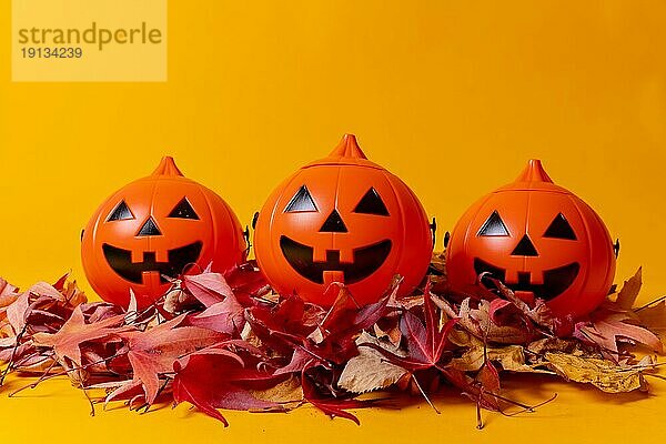 Halloween orange Kürbisse auf einem gelben Hintergrund  verziert mit roten Herbstblättern