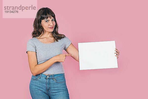 Schöne Frau  die auf ein leeres Whiteboard vor einem rosa Hintergrund zeigt