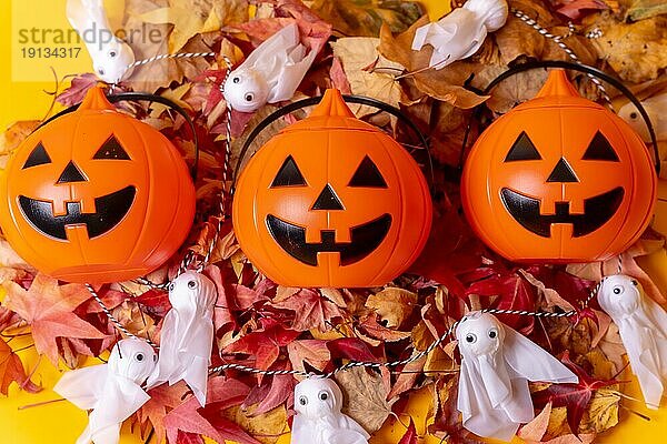 Halloween orange Kürbisse auf einem gelben Hintergrund  verziert mit roten Herbstblättern und kleinen Gespenstern