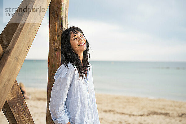 Glückliche reife Frau lächelt an der Rettungsschwimmerhütte am Strand
