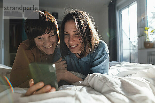 Neugieriges lesbisches Paar  das zu Hause im Bett liegt und sein Smartphone teilt