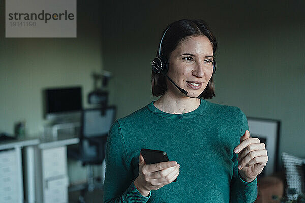 Frau spricht über Headset und hält Smartphone zu Hause