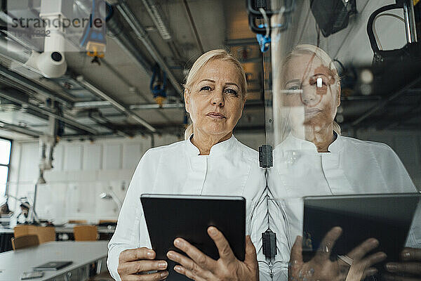 Nachdenklicher Wissenschaftler mit Tablet-PC  der neben einer Glasvitrine steht