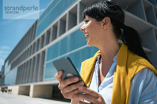 Glückliche Geschäftsfrau  die lacht und ihr Smartphone vor dem Gebäude hält