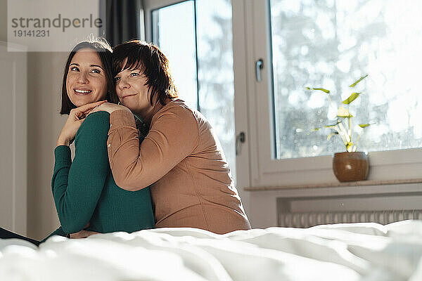 Lesbian couple spending leisure time sitting on bed at home