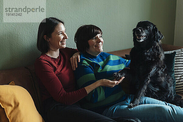 Smiling lesbian couple playing with dog at home