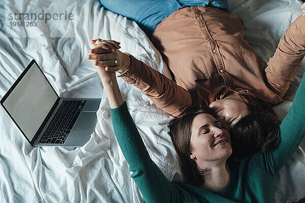 Happy lesbian couple lying down on bed at home