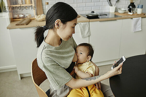 Mother breastfeeding daughter and using smart phone at home