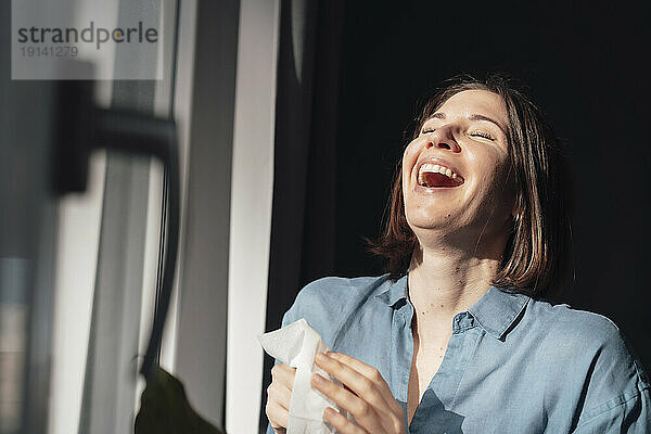 Cheerful woman laughing near window at home