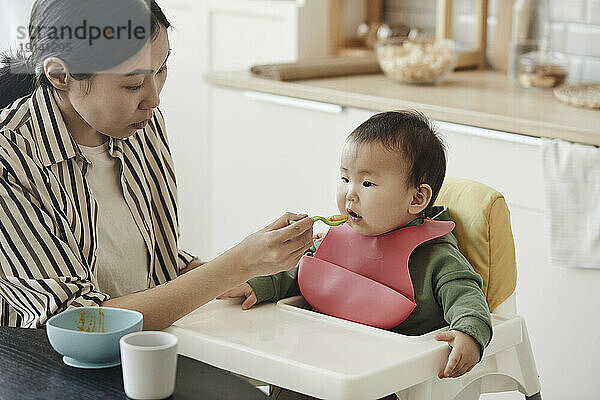Mother feeding fruit puree to daughter at home
