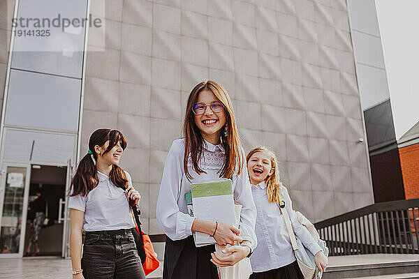 Happy girl with friends standing in front of school building