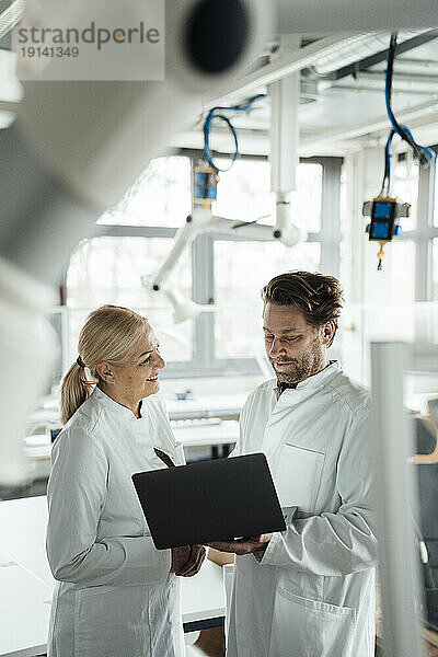 Fröhlicher leitender Wissenschaftler diskutiert mit Kollegen am Laptop im Labor