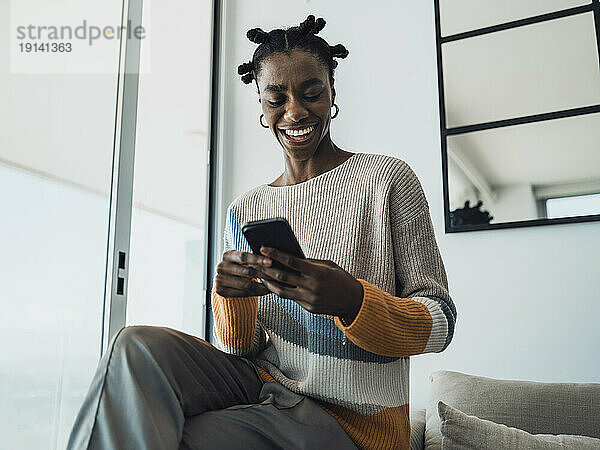Smiling woman reading text messages on smartphone at home