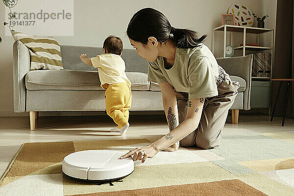 Mother turning on robotic vacuum cleaner looking at daughter at home