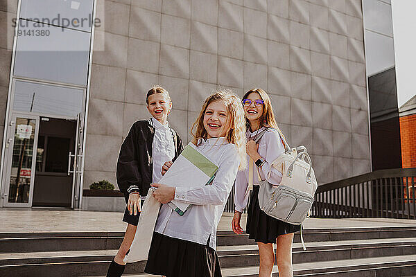 Smiling friends standing in front of school building