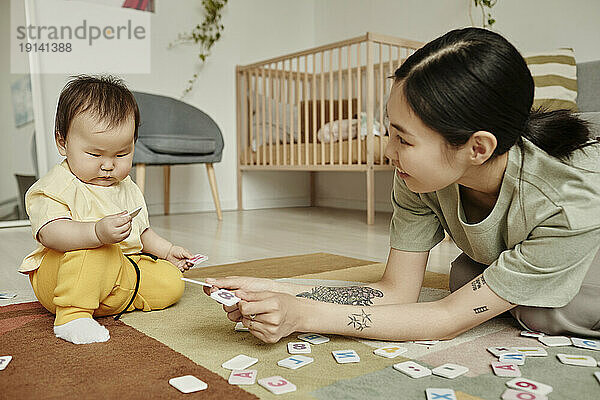 Mutter spielt Worträtsel mit Tochter  die zu Hause auf dem Teppich sitzt