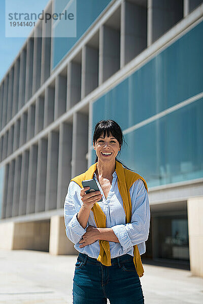 Glückliche Geschäftsfrau mit Smartphone vor dem Gebäude