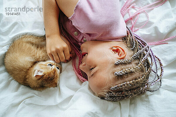 Lächelndes Mädchen  das mit Katze auf dem Bett spielt