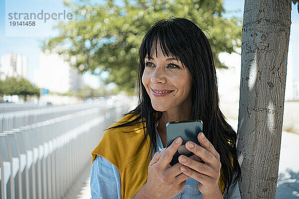 Nachdenklich lächelnde Geschäftsfrau mit Mobiltelefon