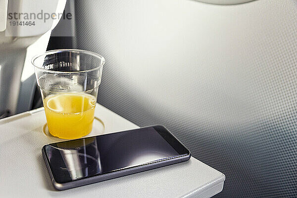 Smartphone und Glas Orangensaft im Flugzeug