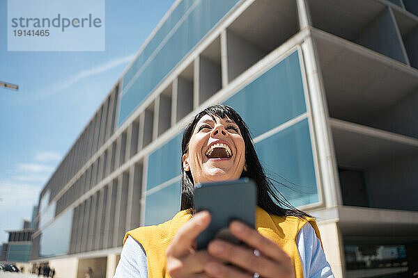 Fröhliche Geschäftsfrau  die vor dem Bürogebäude lacht