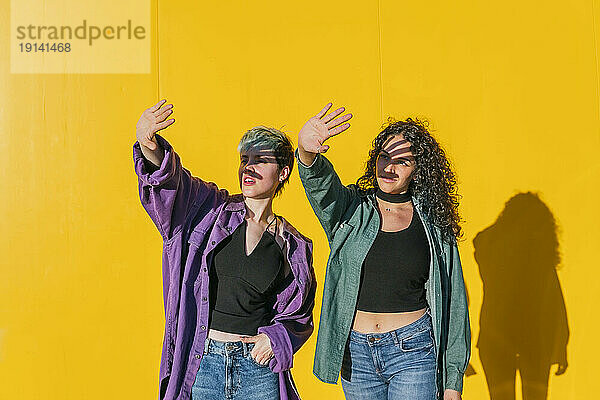 Lesbisches Paar schützt Augen vor Sonnenlicht vor gelber Wand