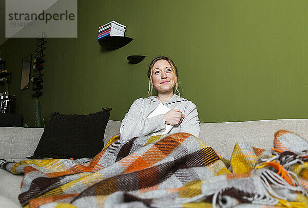 Nachdenkliche junge Frau mit Buch entspannt auf der Couch