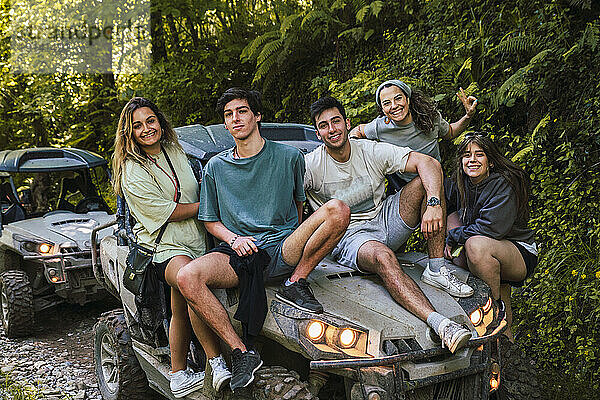 Lächelnde Freunde sitzen auf der Motorhaube eines Buggys im Wald