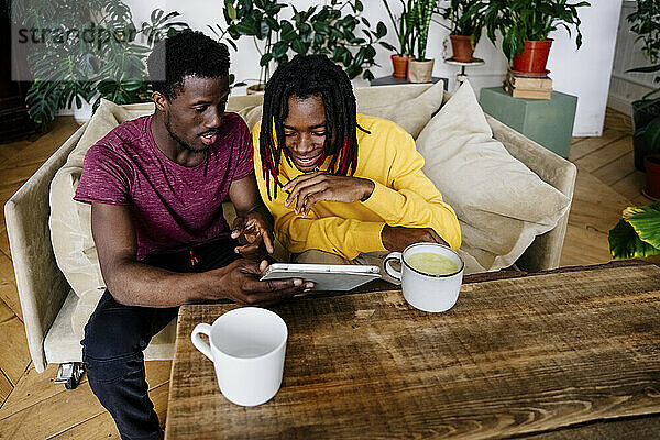 Smiling man sharing tablet PC with friend sitting at home