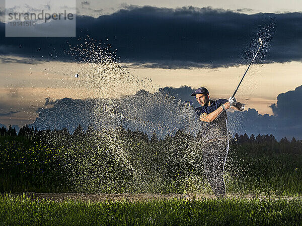 Man playing golf with club sanding on grass at dusk