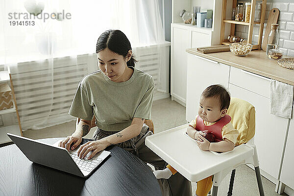 Freelancer mother working on laptop by daughter at home