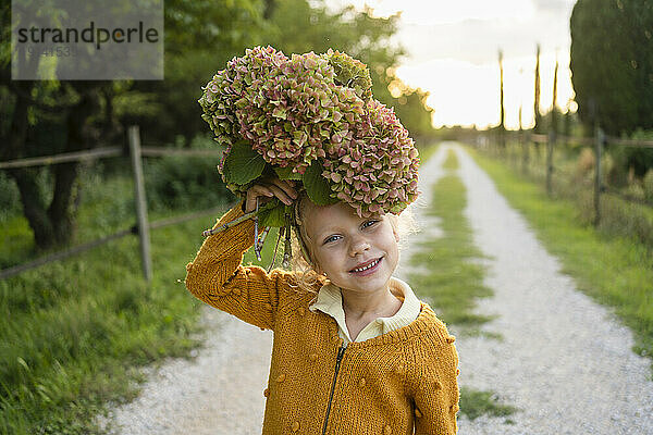 Smiling girl holding Hydrangea flower over head on footpath