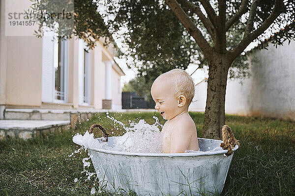 Kleiner Junge nimmt ein Bad und spritzt Wasser in die Wanne im Hinterhof