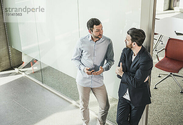 Business colleagues discussing leaning on glass door in office