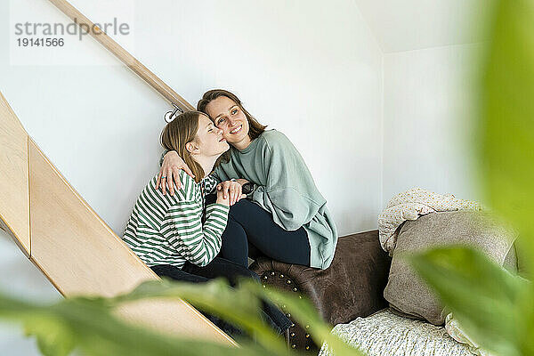 Mother embracing daughter sitting near staircase at home