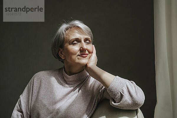 Mature woman leaning on couch with eyes closed at home