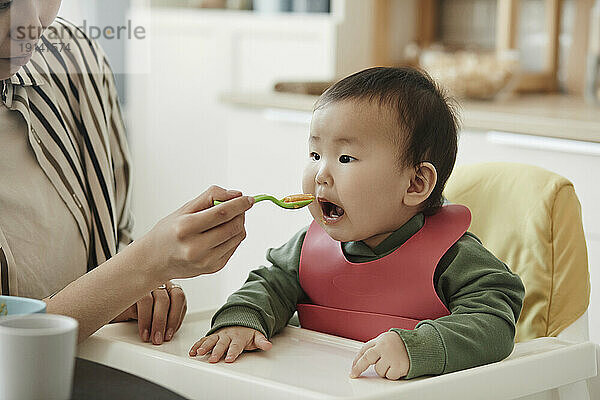 Daughter eating fruit puree fed by mother at home