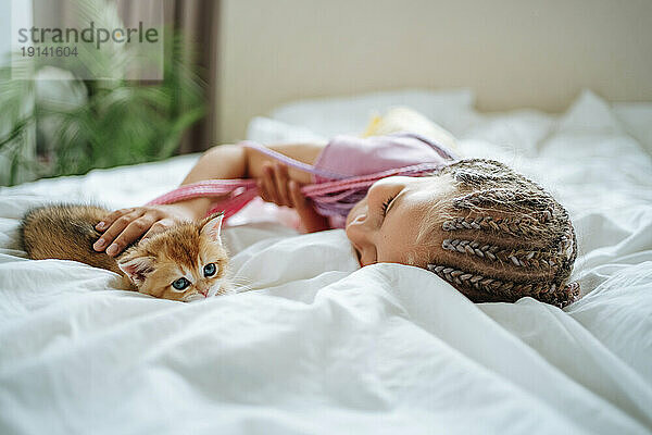 Girl playing with ginger kitten on bed