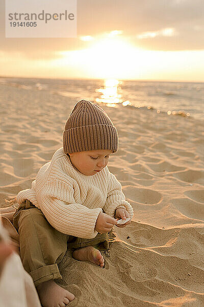 Netter Junge mit Strickmütze spielt am Strand