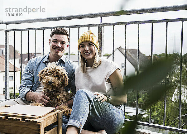 Glückliches junges Paar sitzt mit Hund auf dem Balkon